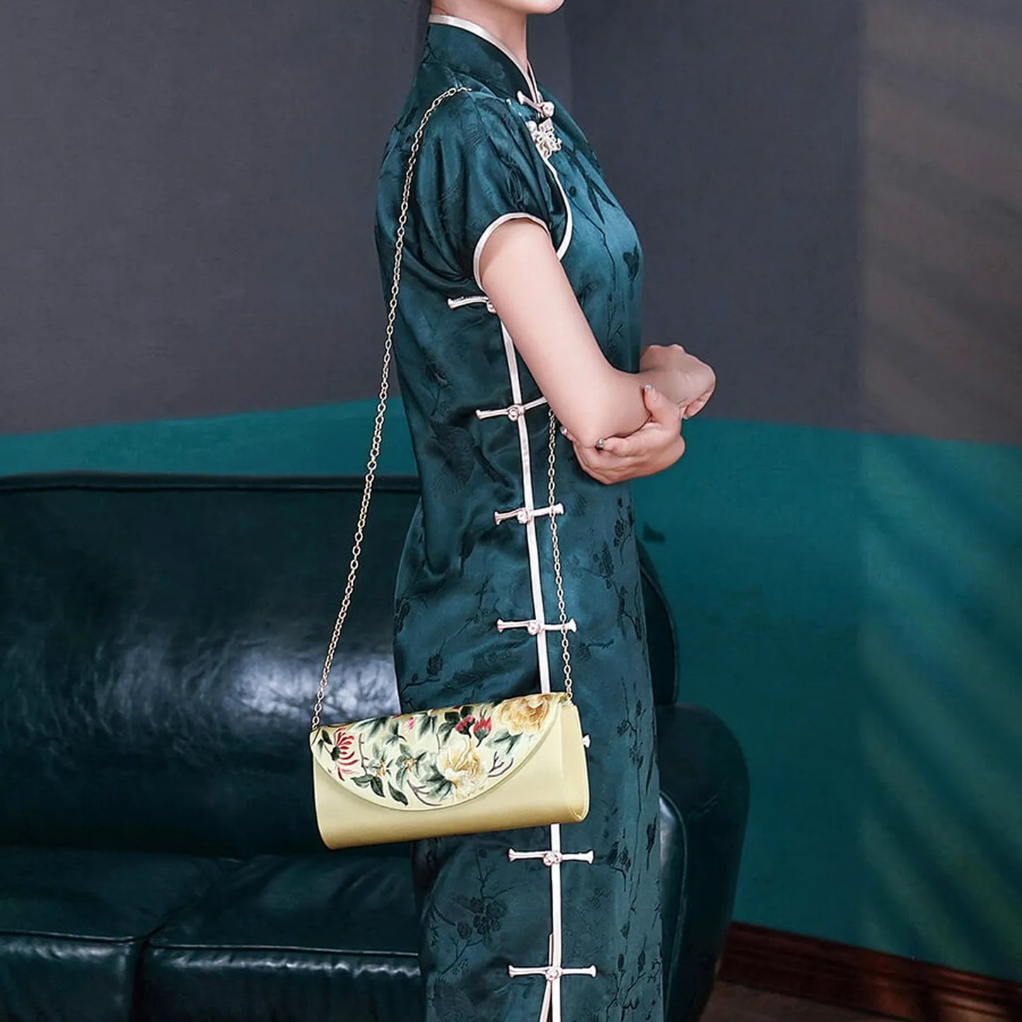 Woman in a green traditional outfit holding a yellow handbag in a room with a blue couch and framed pictures.