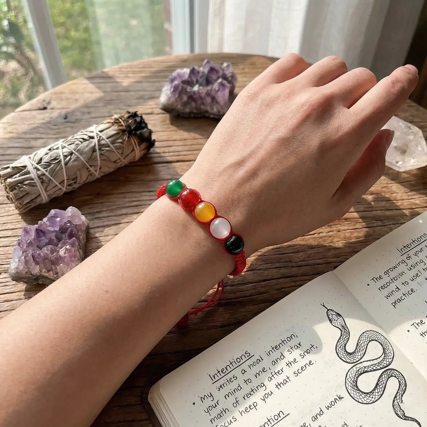 Hand wearing a colorful beaded bracelet on a wooden surface with crystals and a book.