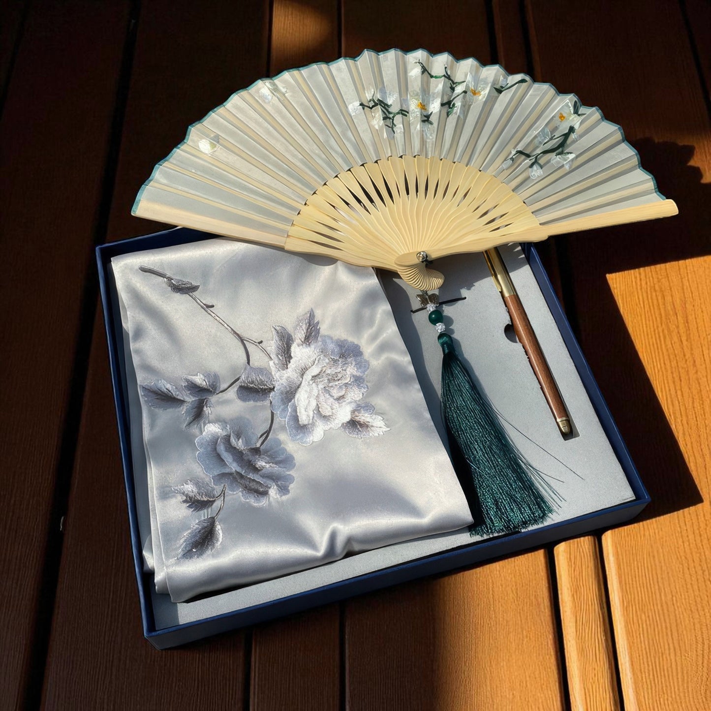 Decorative fan with floral design on a matching pouch in a box on a wooden surface
