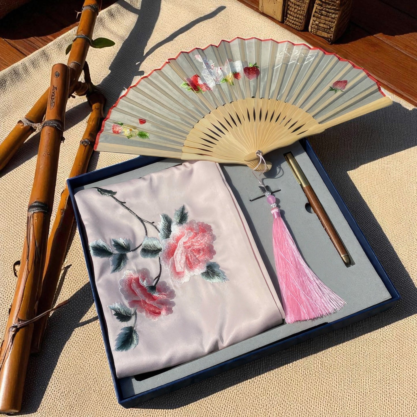 Embroidered fabric with floral design, fan, and bamboo sticks on a textured surface
