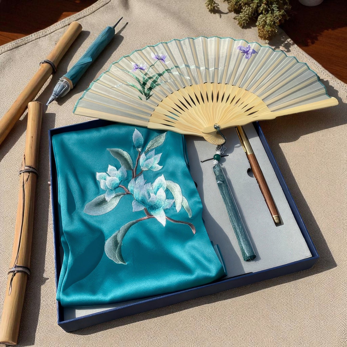 Teal embroidered fabric with floral design, bamboo sticks, and a hand fan on a beige surface.