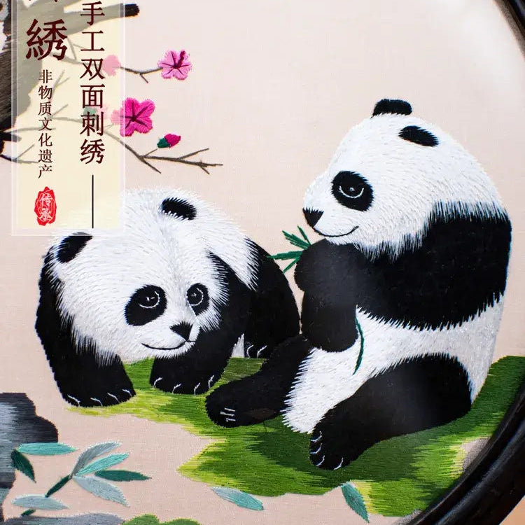 Embroidery of two pandas on a circular frame with floral decorations.