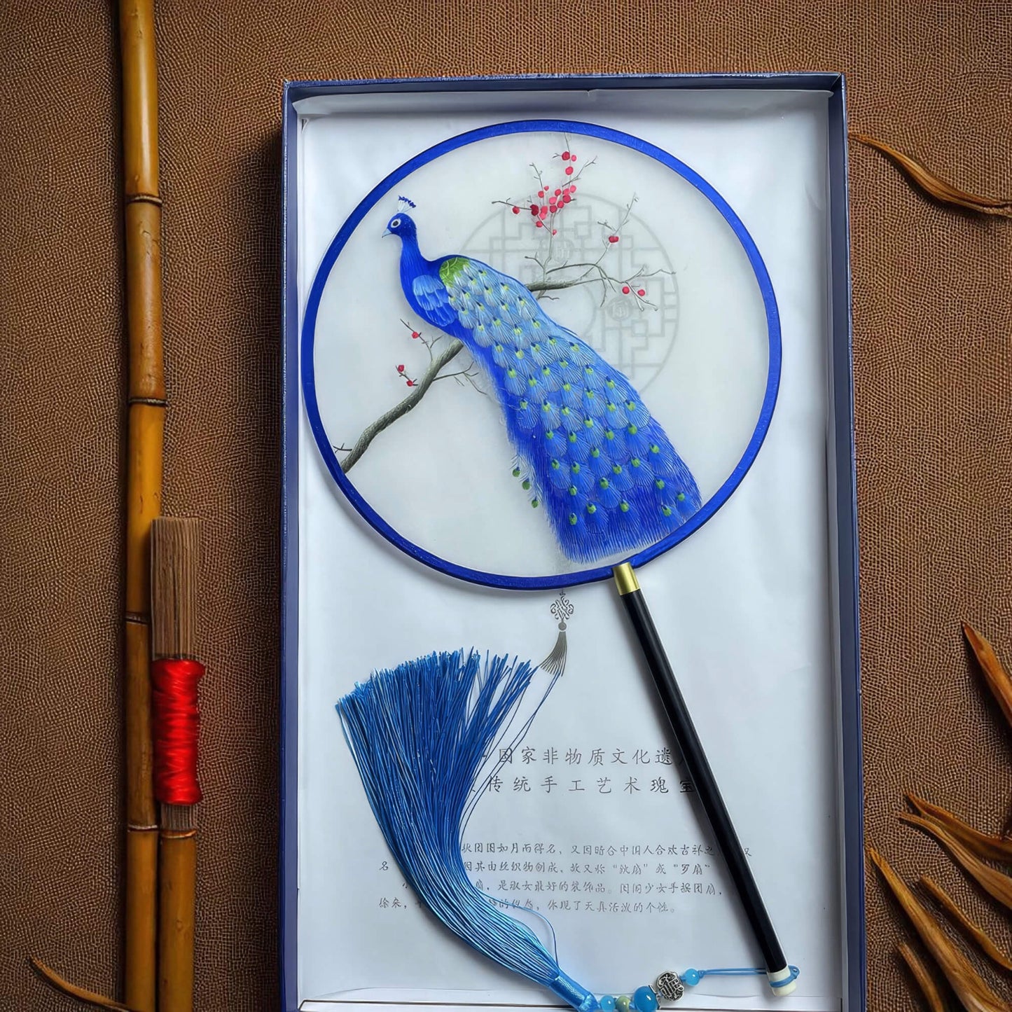 Decorative fan with peacock design in a box on a brown background