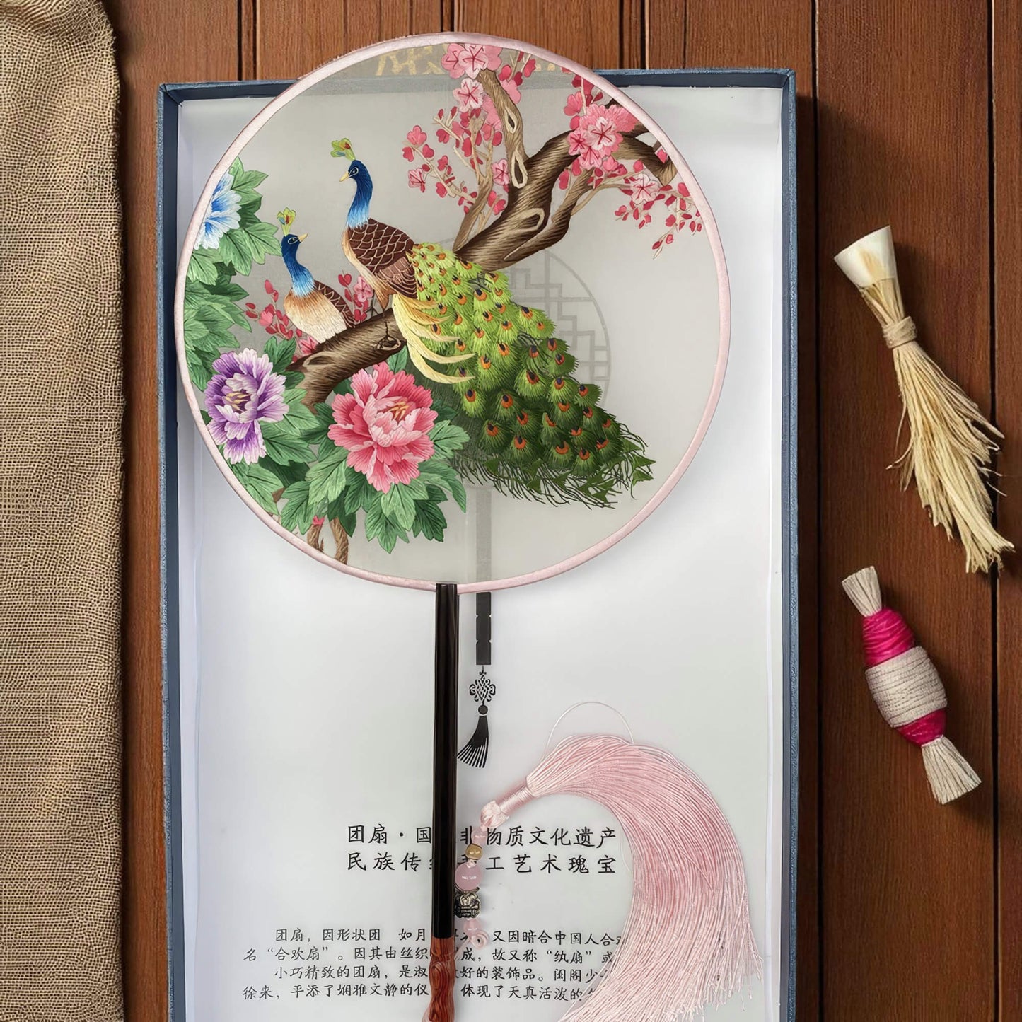 Decorative round fan with peacocks and flowers on a wooden surface