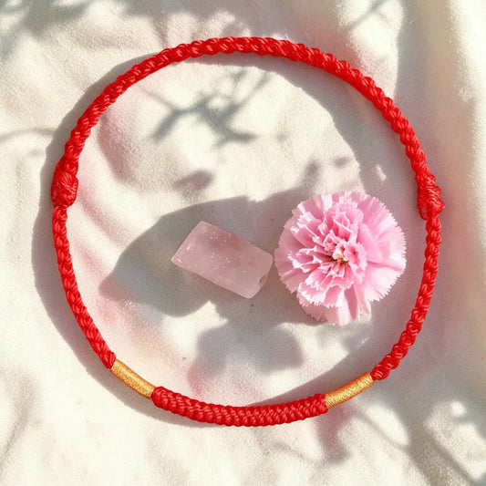 Red bracelet with gold accent on a white surface with a pink flower and crystal.