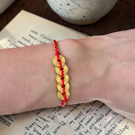 Gold bracelet with red cord on a wrist, placed on an open book.