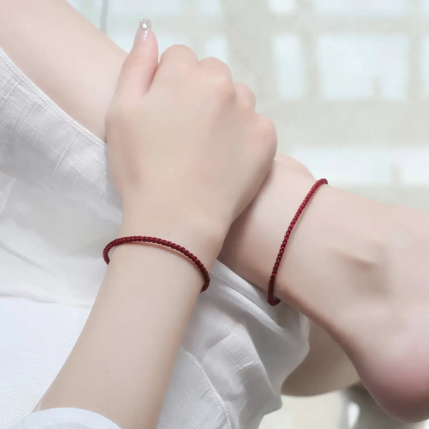 Two hands wearing red string bracelets on a white background