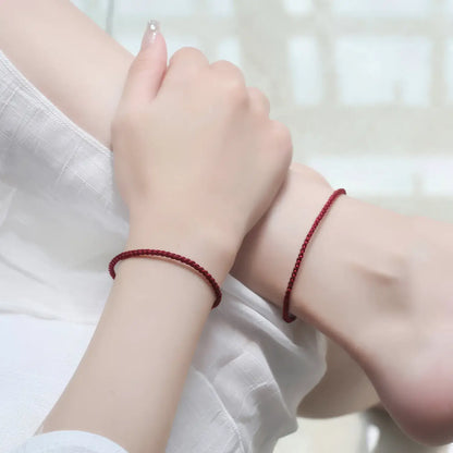 Two hands wearing red string bracelets on a white background