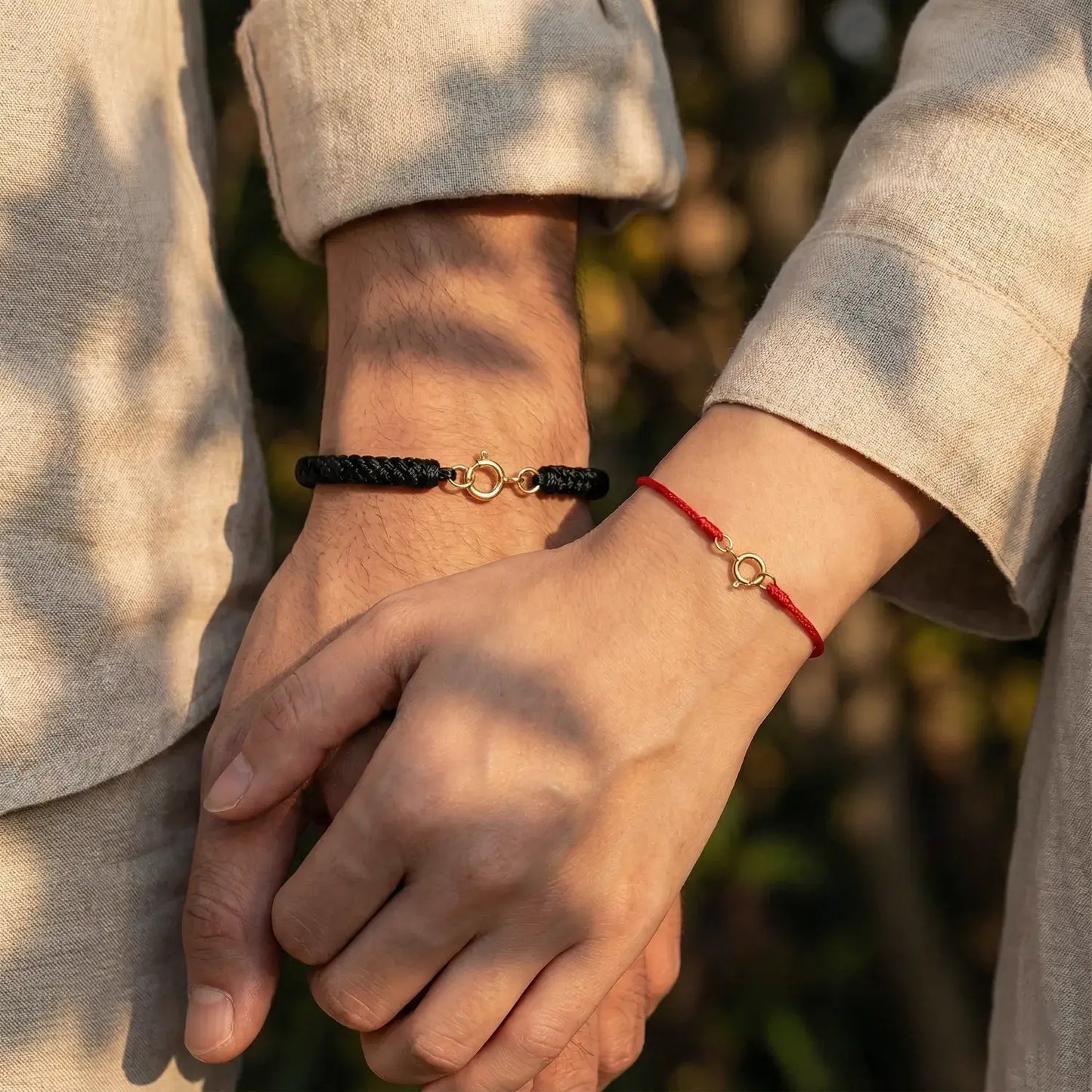 Two people holding hands with matching bracelets against a blurred natural background