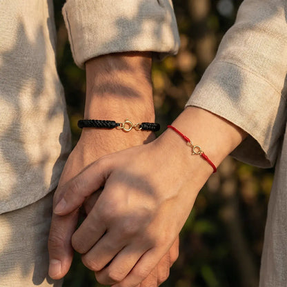 Two people holding hands with matching bracelets against a blurred natural background