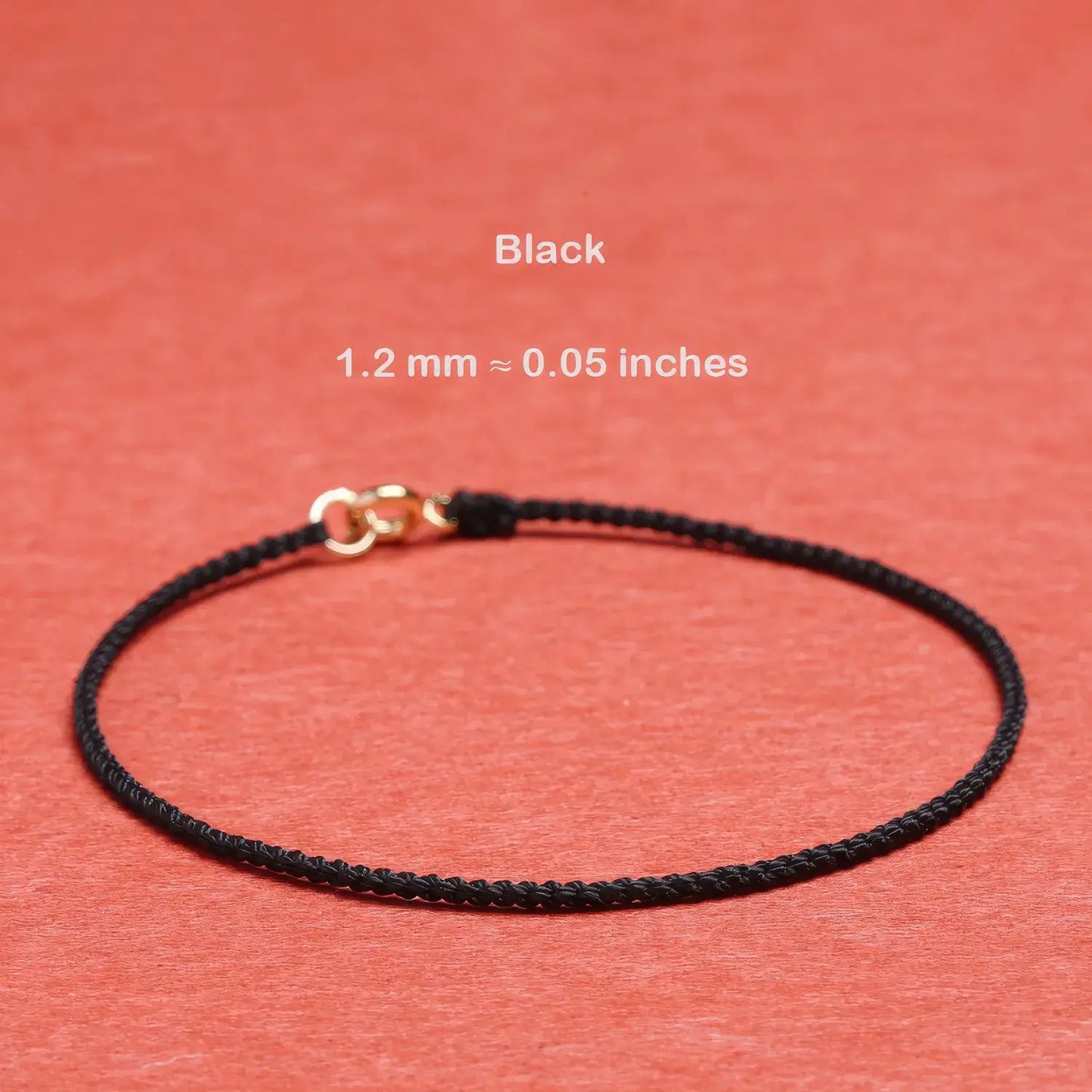 Black cord bracelet with gold clasp on a red background