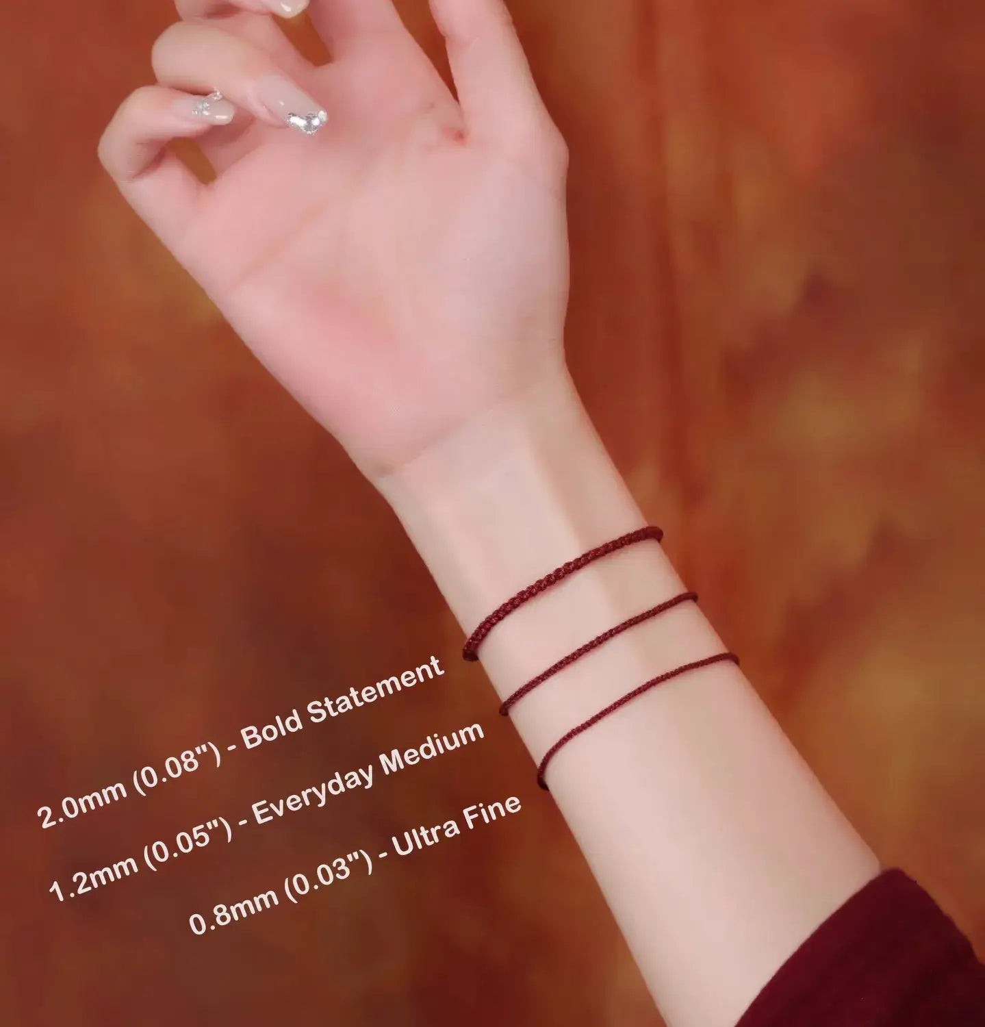 Hand wearing two red thread bracelets with size labels on a blurred background