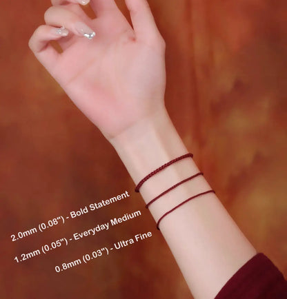 Hand wearing two red thread bracelets with size labels on a blurred background