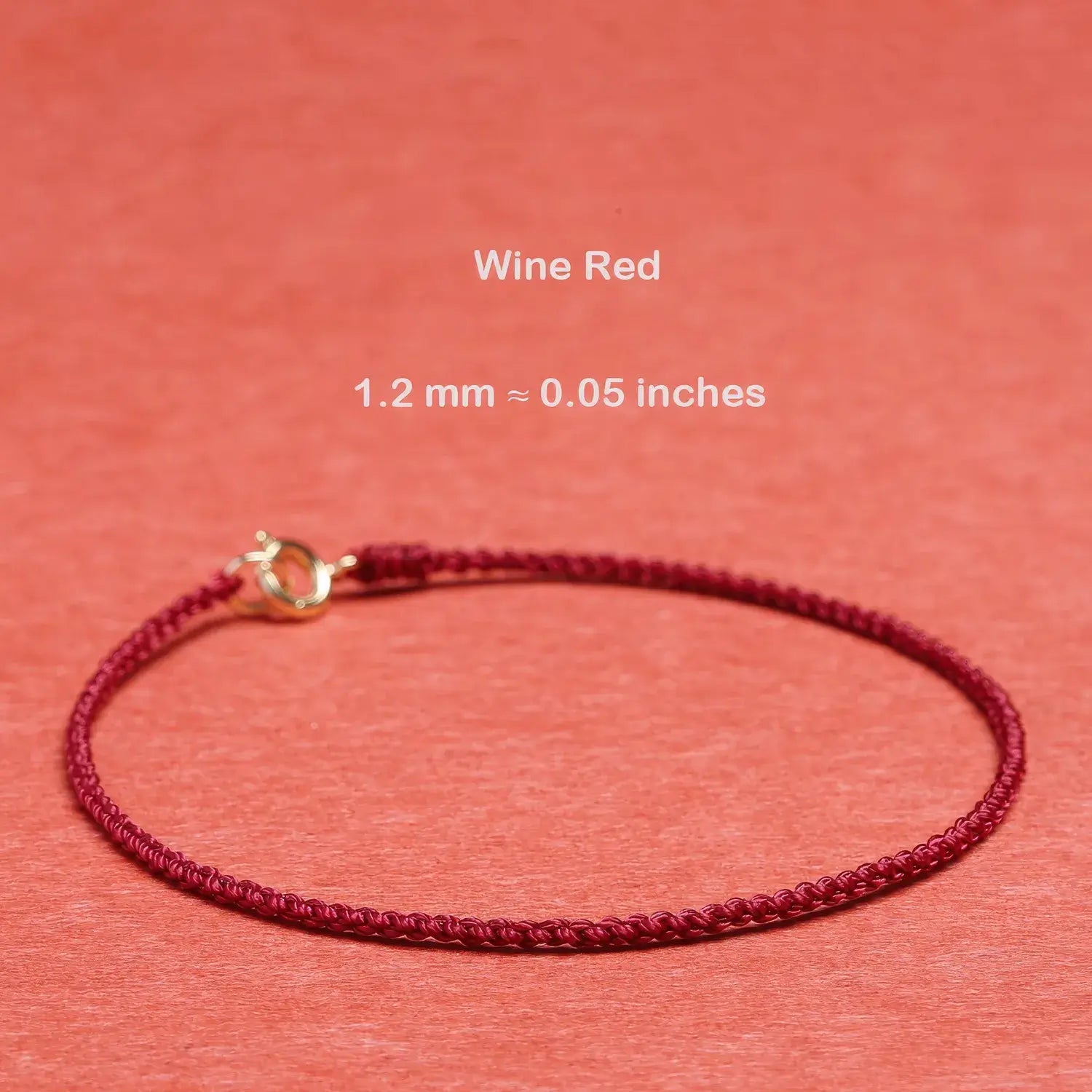 Wine red bracelet with gold clasp on a coral background