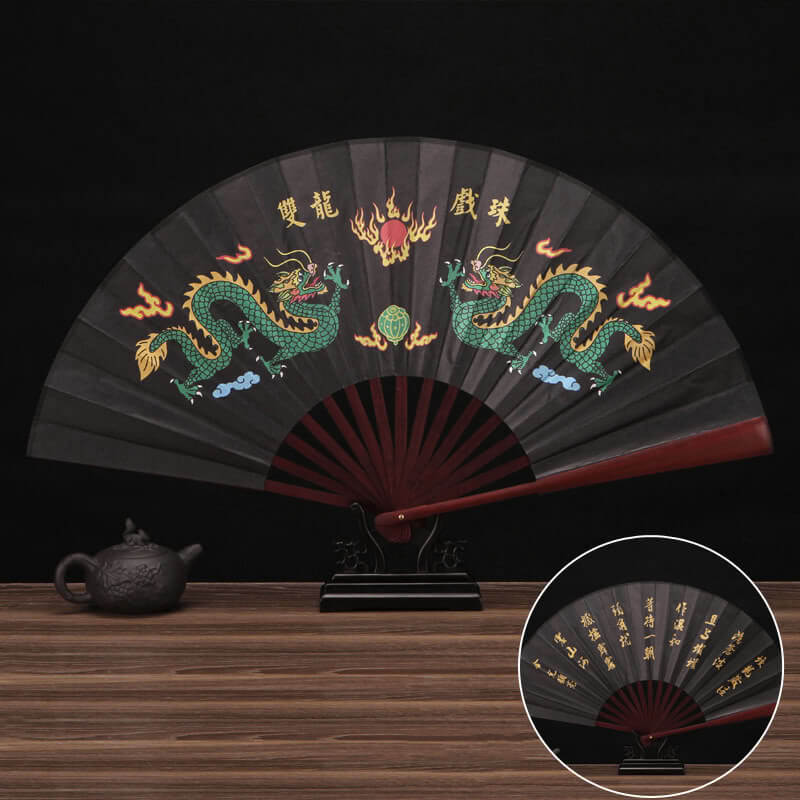 Decorative fan with dragon design on a wooden surface with a teapot.