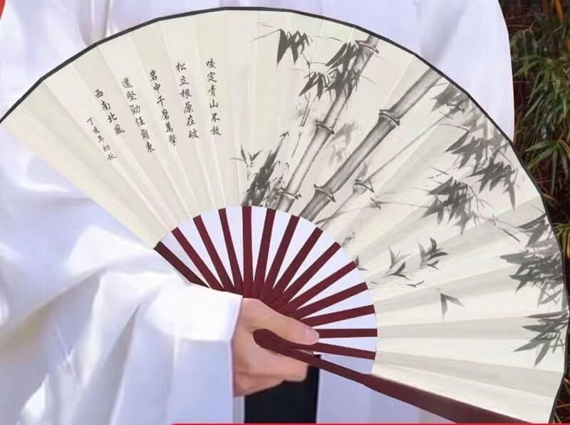 Hand holding a traditional folding fan with bamboo design and calligraphy.