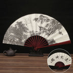 Traditional Chinese folding fan with landscape design on a wooden table.