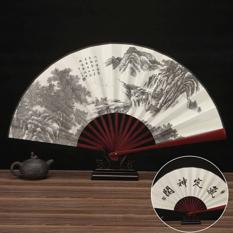 Traditional Chinese folding fan with landscape design on a wooden table.