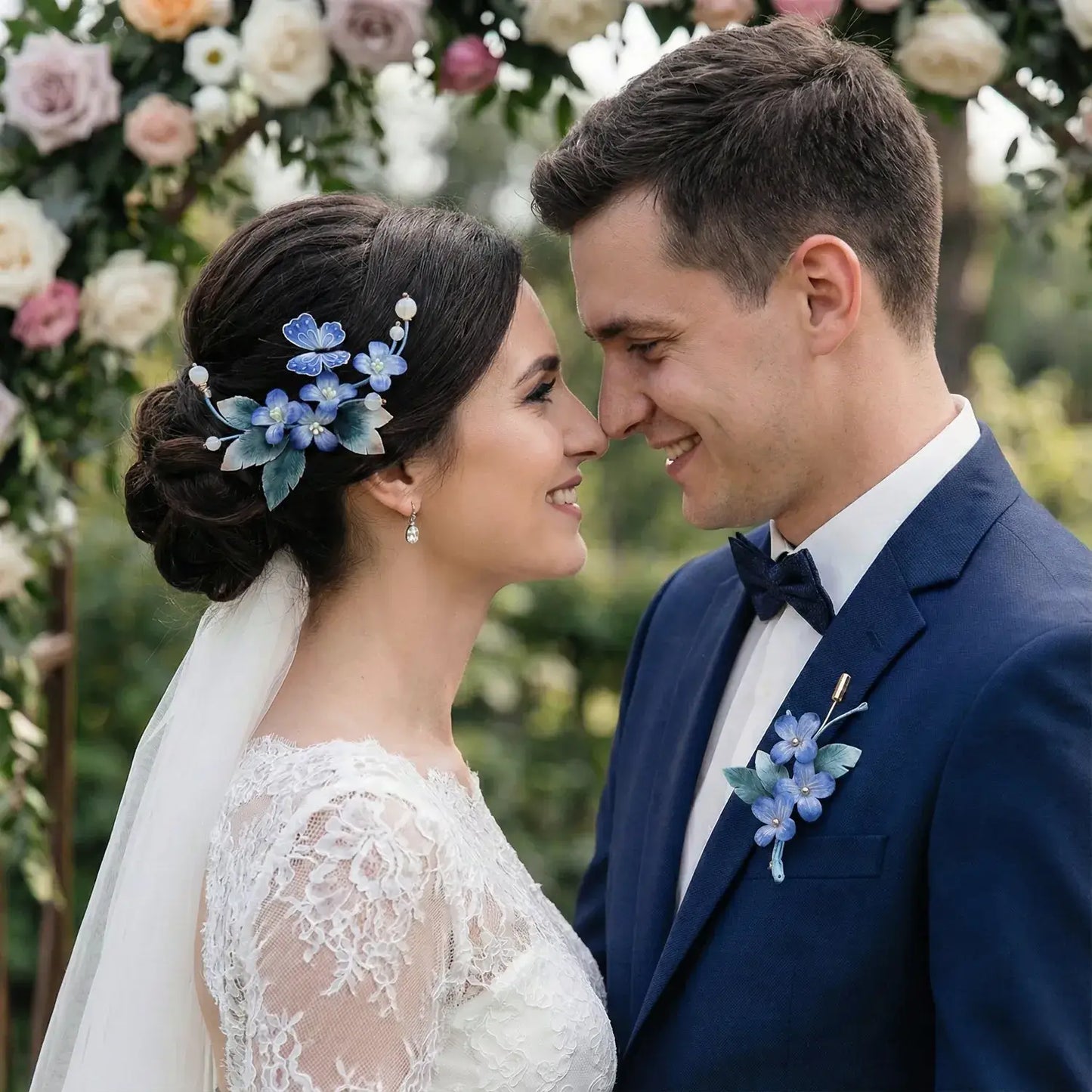 Couple in wedding attire with floral decorations, standing in front of a floral arch.