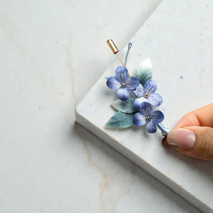 Blue floral hair clip on a marble surface with a hand holding it.