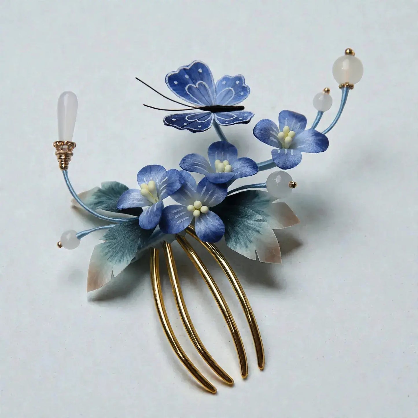 Decorative hair comb with blue flowers and gold accents on a light gray background