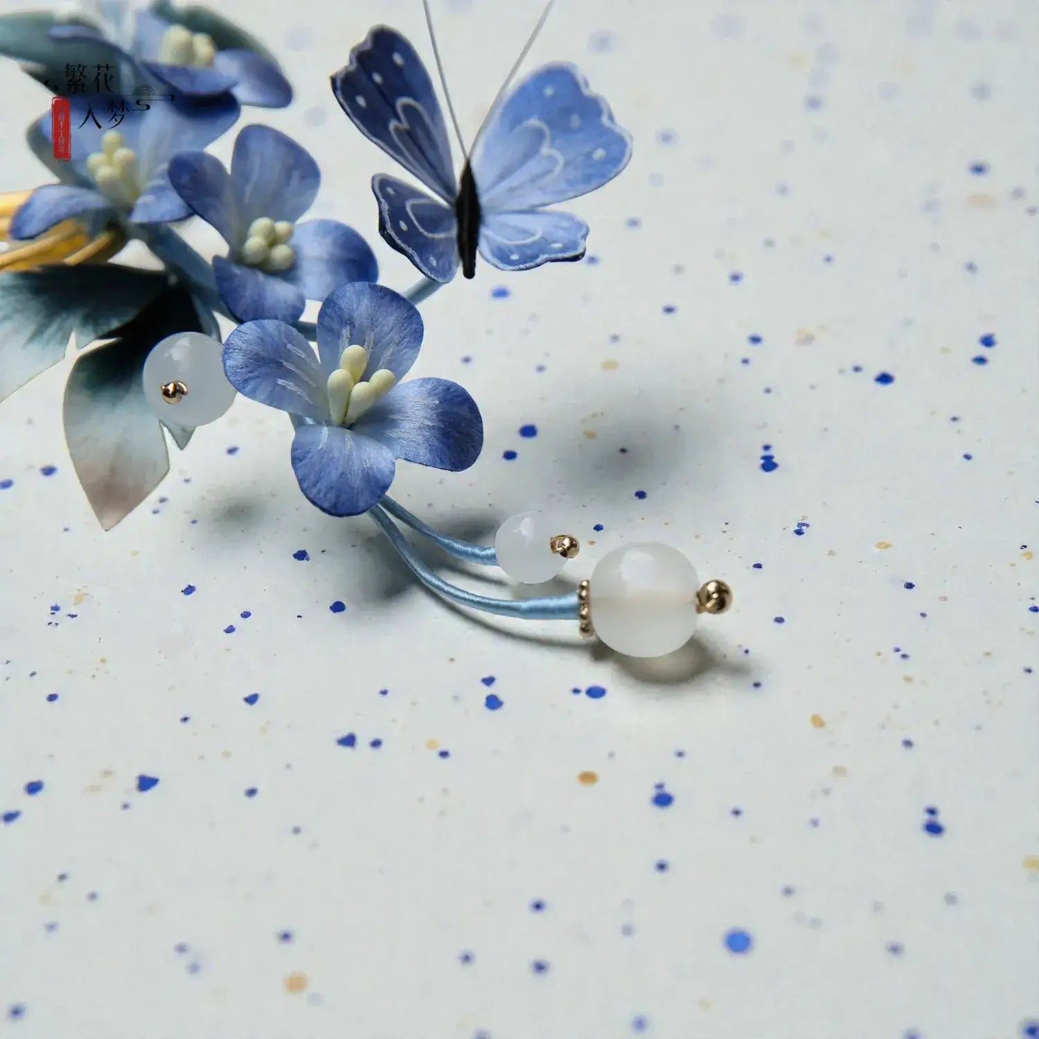 Earring with blue floral design and butterfly on a speckled background