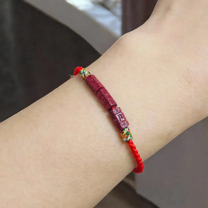 A red Chinese-style cord bracelet with carved red beads and small gold and green decorative accents, shown worn on a person's wrist.