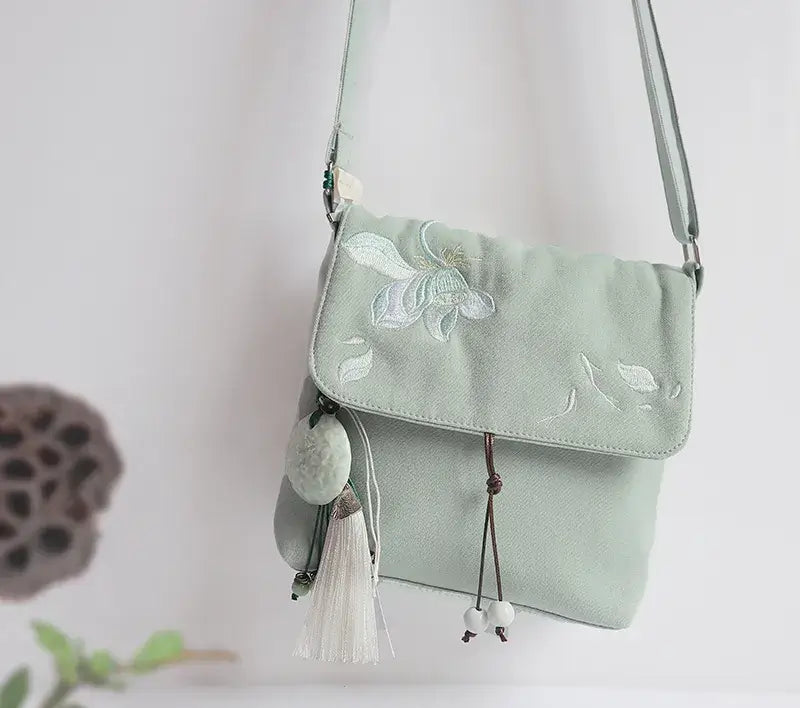 Light green handbag with floral embroidery and tassels on a white background