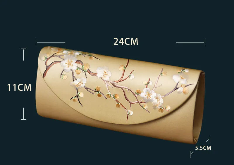 Gold clutch bag with floral design and measurements on a dark background