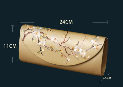 Gold clutch bag with floral design and measurements on a dark background