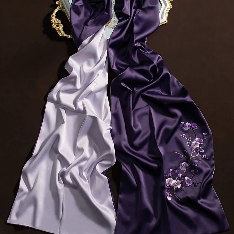 Two satin scarves, one white and one purple with floral embroidery, on a dark background.