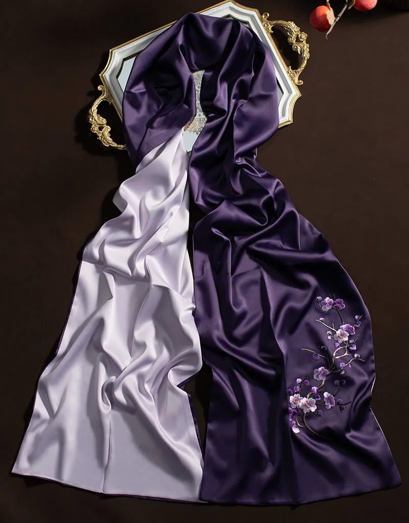 Two satin scarves, one white and one purple with floral embroidery, on a dark background.