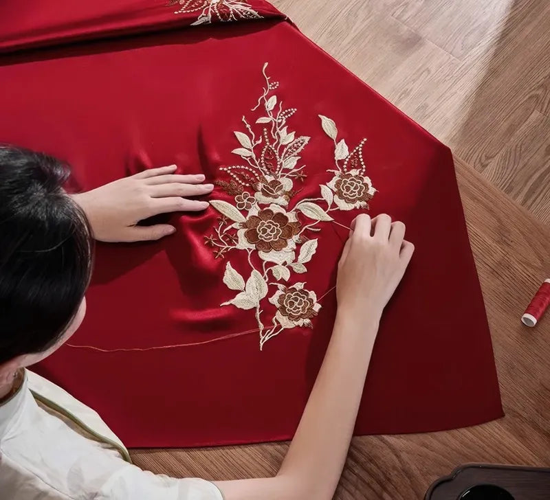 Person working on embroidery on a red fabric with floral patterns