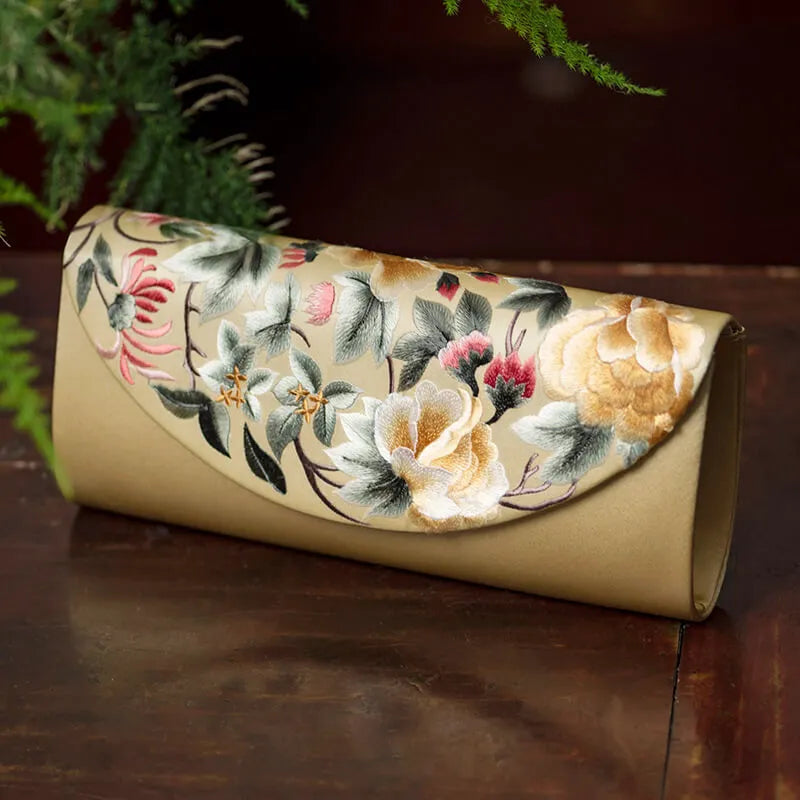 Floral embroidered clutch bag on a wooden surface with greenery in the background