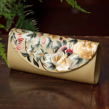 Floral embroidered clutch bag on a wooden surface with greenery in the background