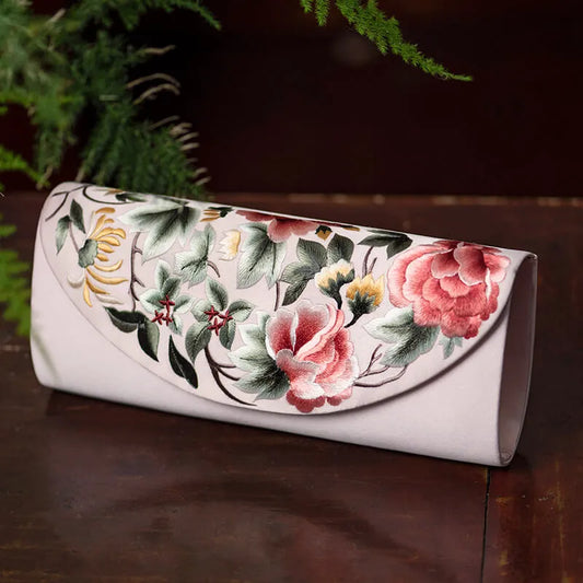 Floral embroidered clutch on a wooden surface with greenery in the background