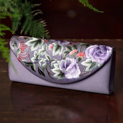Floral embroidered clutch bag on a dark surface with greenery in the background