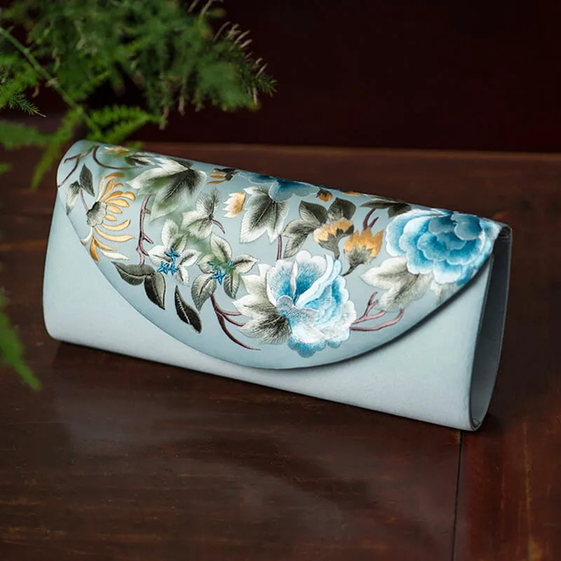 Floral embroidered clutch bag on a wooden surface with greenery in the background
