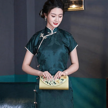 Woman in a green traditional dress holding a gold clutch against a dark background