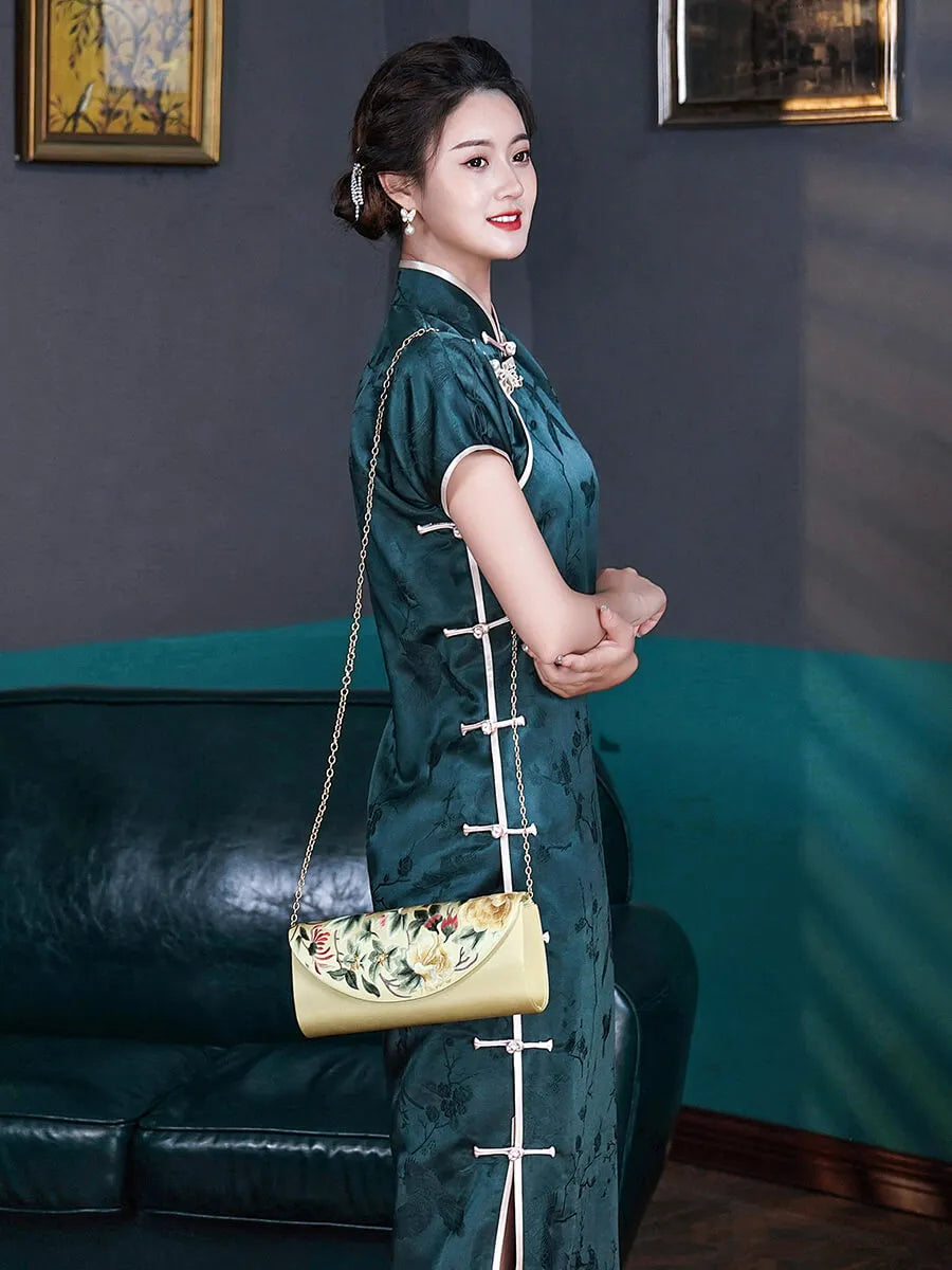 Woman in a green traditional outfit holding a yellow handbag in a room with a blue couch and framed pictures.