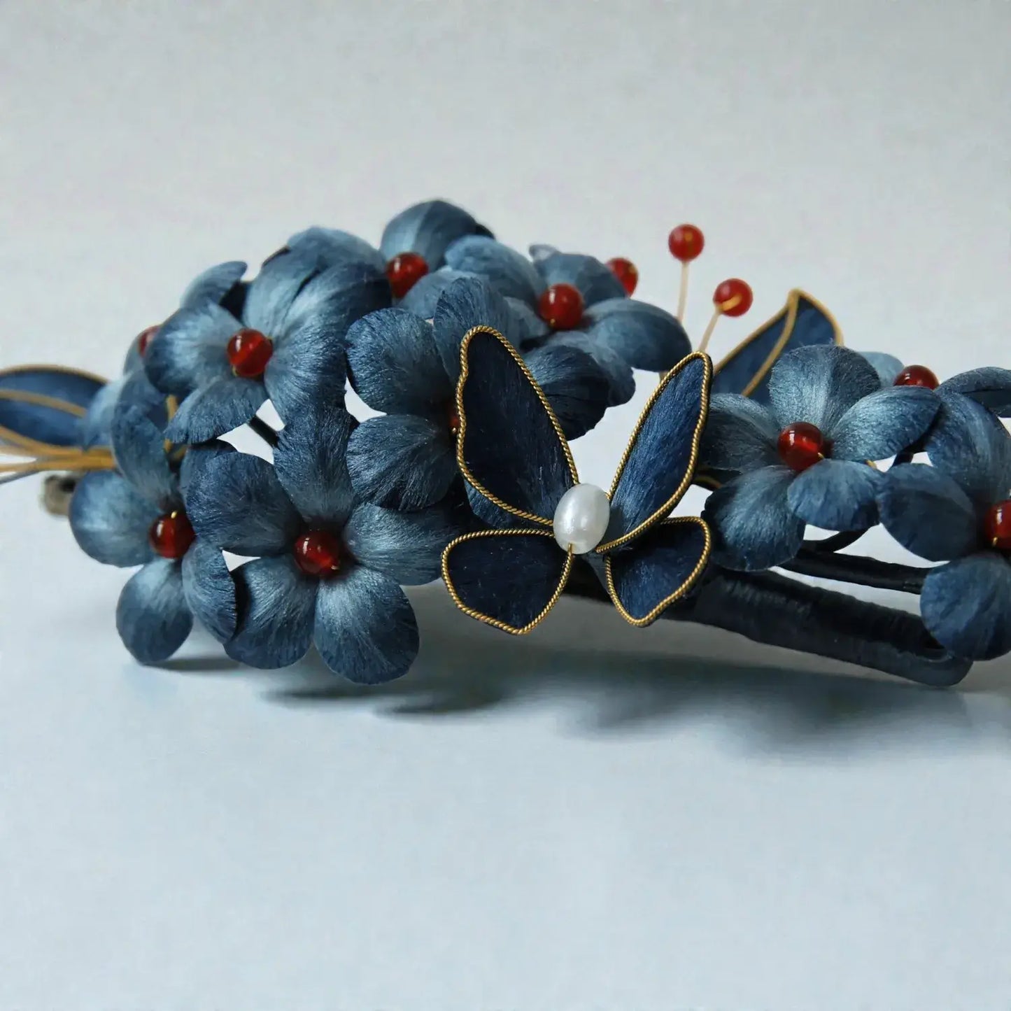 Blue floral hair accessory with a butterfly and pearl detail on a light gray background