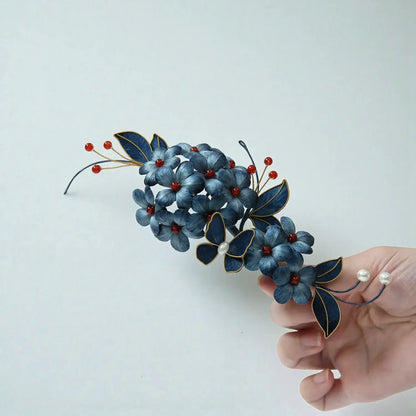 Decorative hair accessory with blue flowers and red berries held by a hand against a light blue background