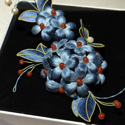 Decorative brooch with blue flowers and red berries on a black background