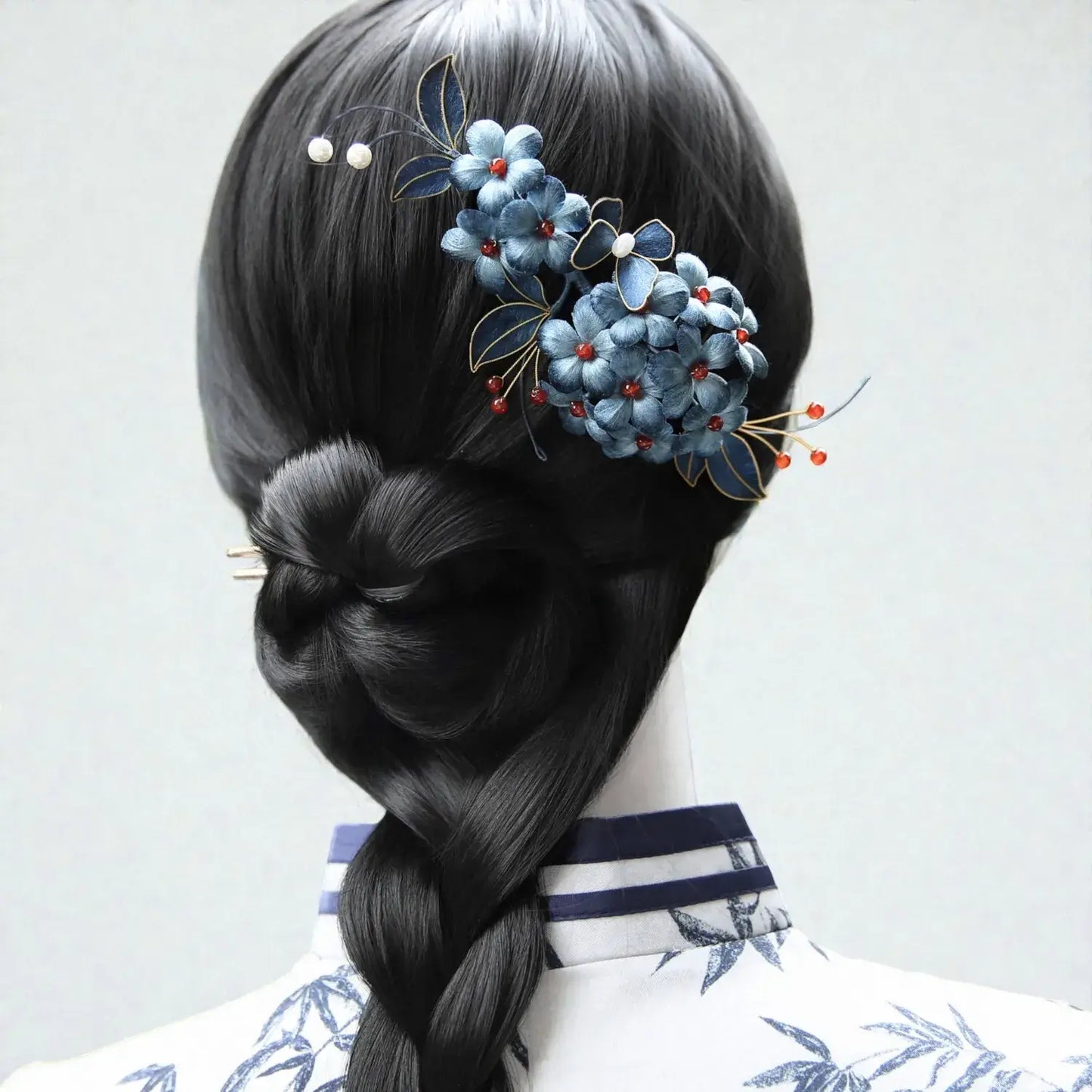 Hair styled in a braid with decorative hairpin featuring blue flowers and red berries on a plain background.