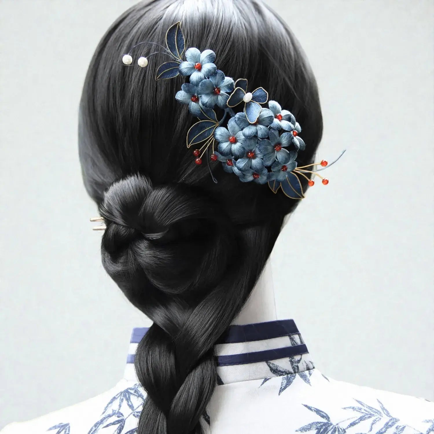 Hair styled in a braid with decorative hairpin featuring blue flowers and red berries on a plain background.