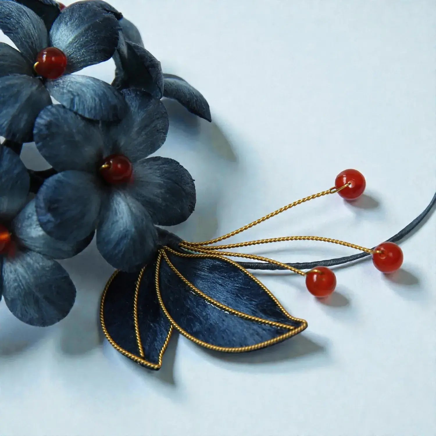 Blue floral hair accessory with red beads and gold accents on a white background