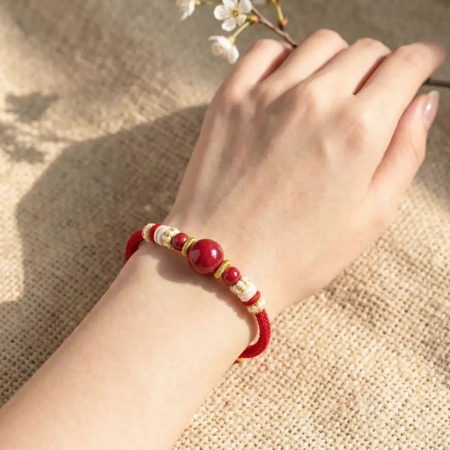 Hand wearing a red beaded bracelet on a textured surface with a branch of flowers.