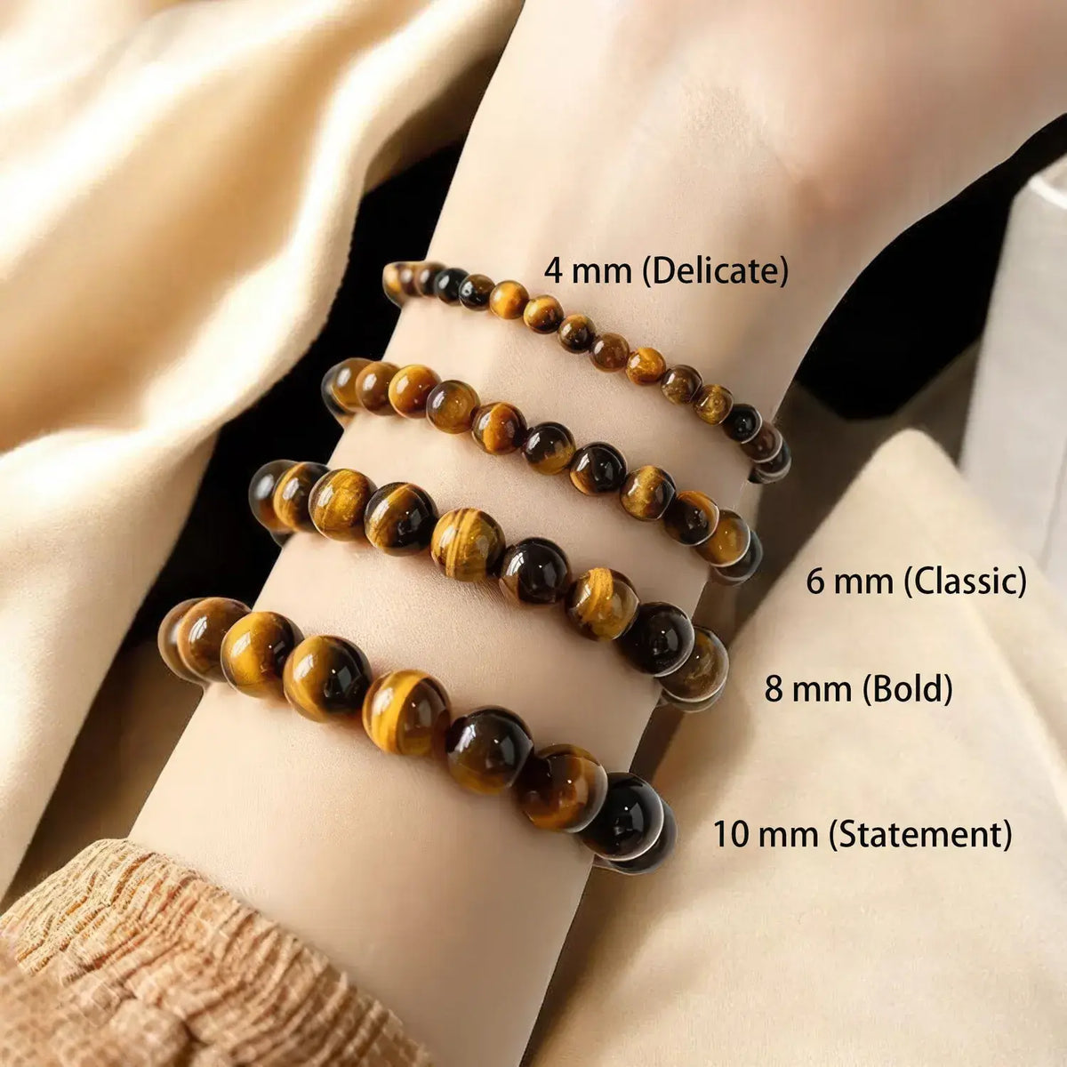 Four beaded bracelets made of tiger's eye stone shown on a person's wrist, labeled by size: 4 mm (Delicate), 6 mm (Classic), 8 mm (Bold), and 10 mm (Statement).
