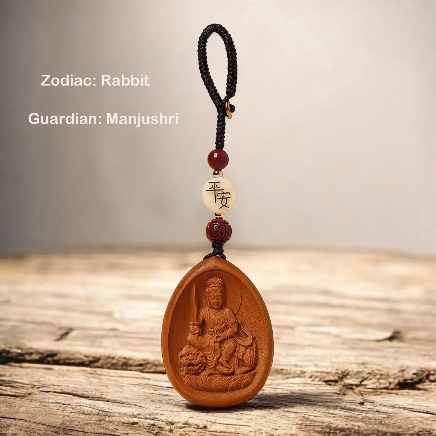 Wooden pendant with a figure and beads on a wooden surface, labeled 'Zodiac: Rabbit, Guardian: Manjushri'.