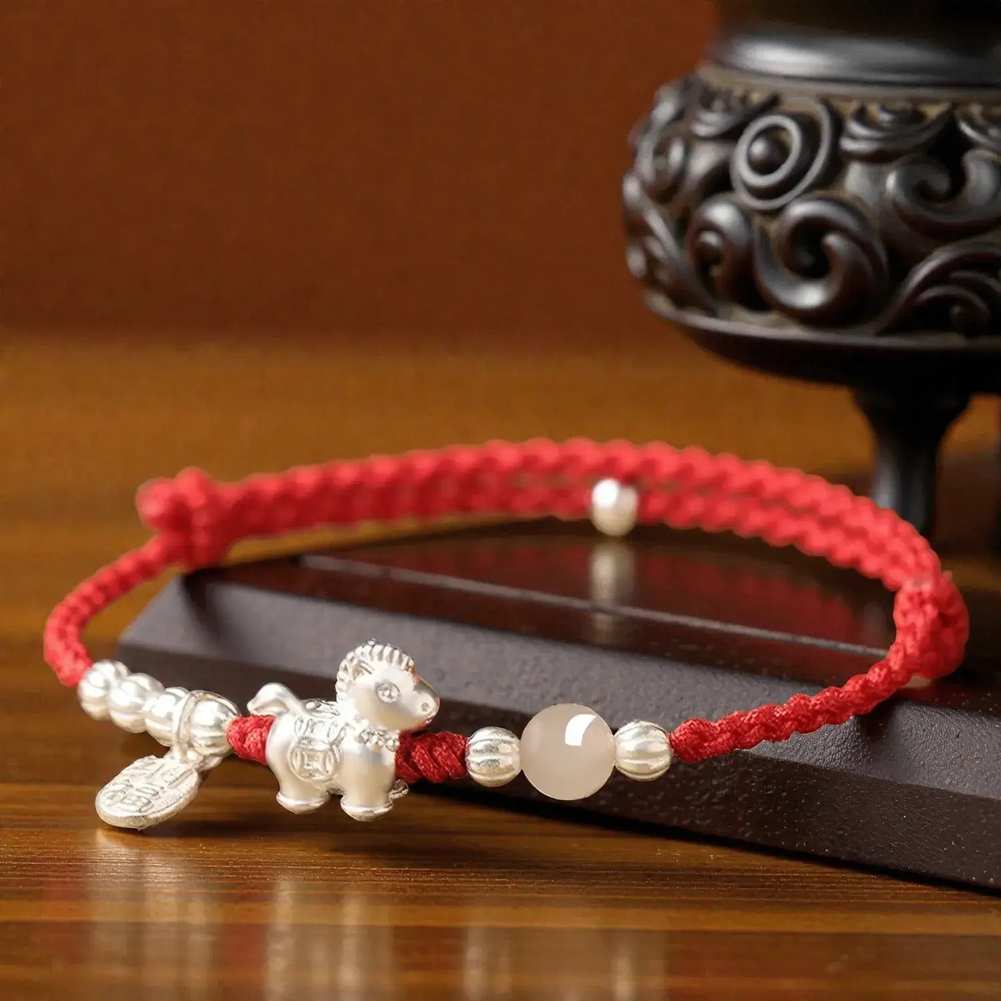 Red string bracelet with silver dog charm and beads on a wooden surface
